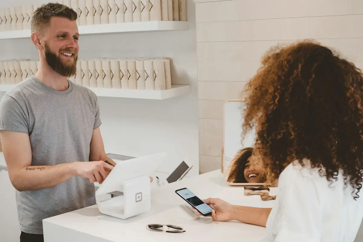 Lojista sorridente atendendo uma cliente que paga pelo celular