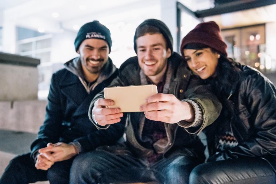 Três amigos sorrindo enquanto olham juntos para a tela de um celular