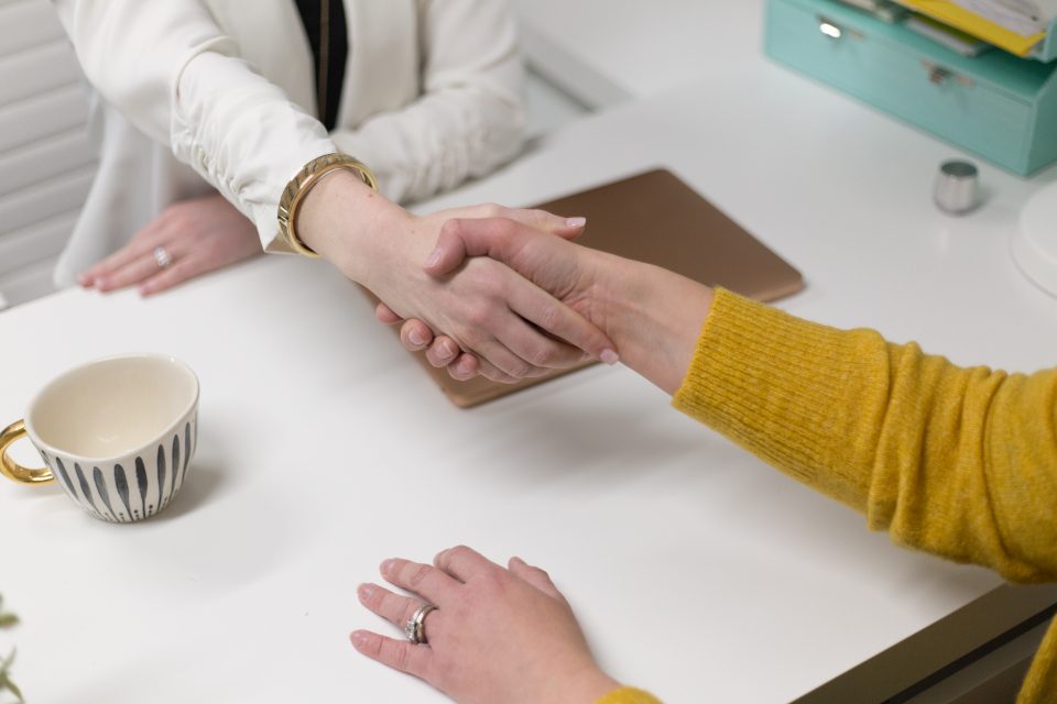 Duas pessoas apertando as mãos sobre uma mesa de reunião