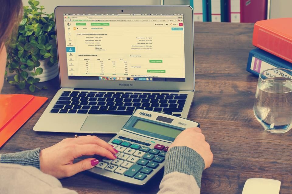 Mãos fazendo contas numa calculadora ao lado de um notebook aberto com uma planilha