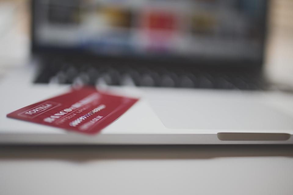 Mão segurando um cartão de crédito em frente a um notebook aberto