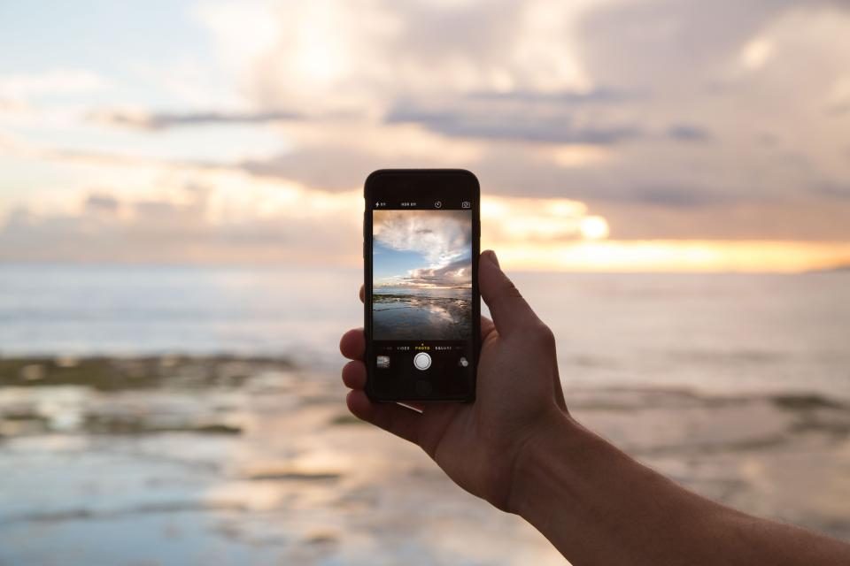 Mão segurando o celular para fotografar o mar