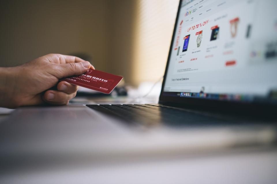 Mão segurando um cartão de crédito diante de um notebook com uma loja virtual aberta na tela