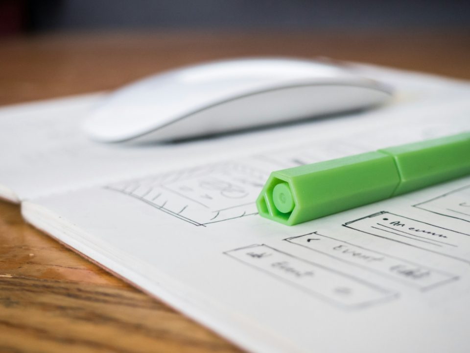 Caderno com esboços de telas de site, um marca-texto verde e um mouse sobre a mesa