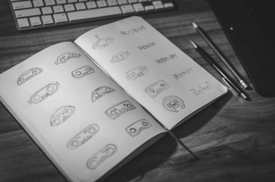 Caderno aberto com esboços de logotipos e lápis ao lado
