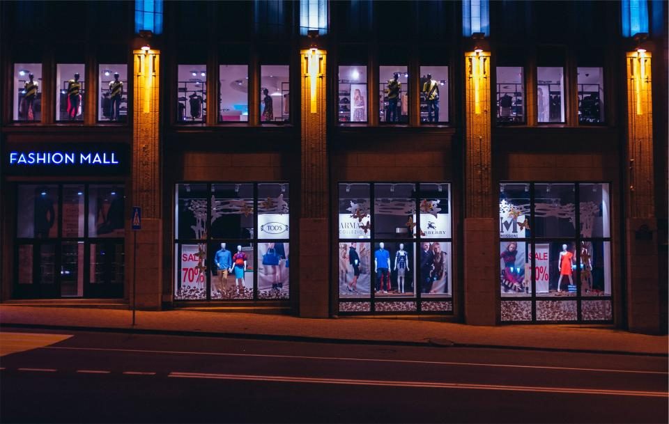 Fachada iluminada de uma loja de roupas, vista da rua à noite