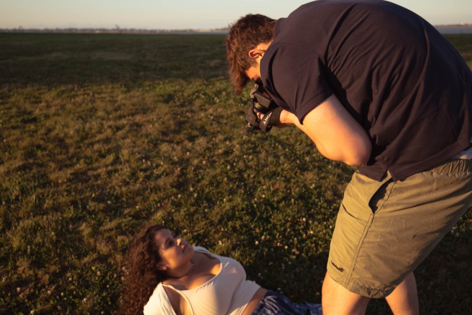 Fotógrafo inclinado sobre o campo, fazendo fotos ao ar livre no fim da tarde