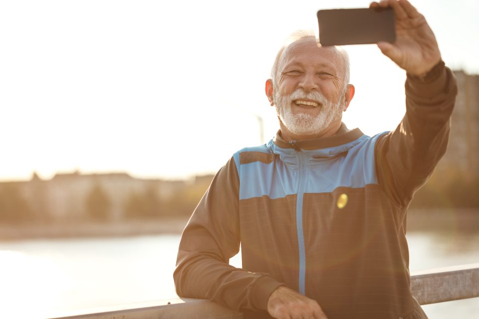 Homem idoso sorrindo enquanto usa o celular ao ar livre