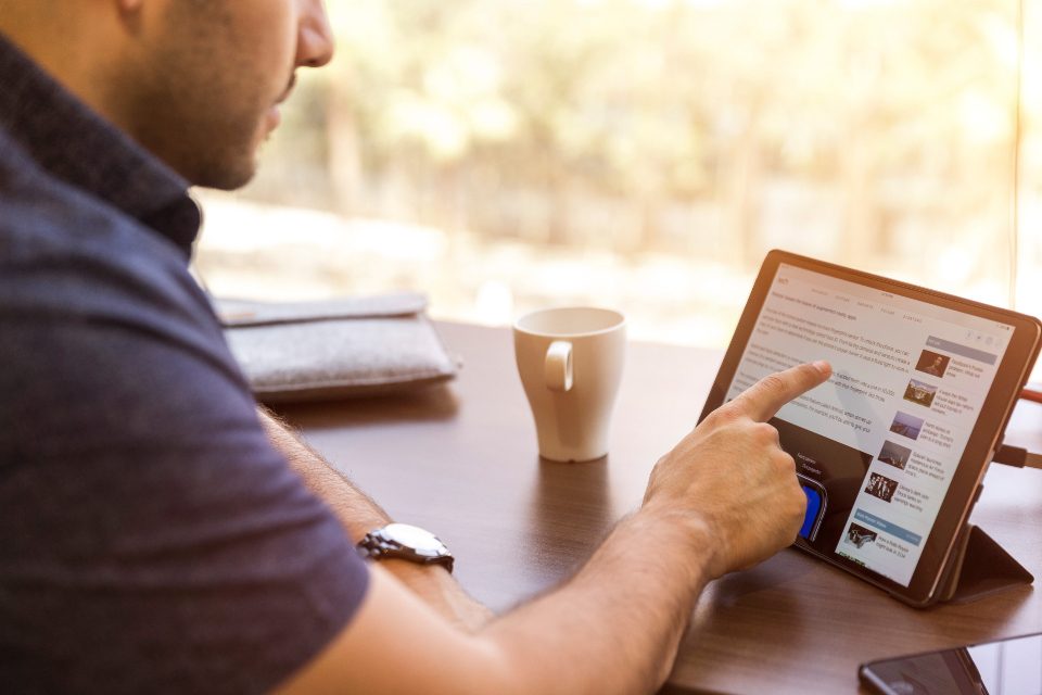 Homem lendo um artigo no tablet sentado à mesa