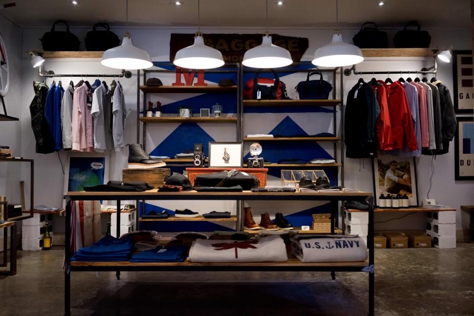 Interior de uma loja de roupas com araras, prateleiras e luminárias pendentes