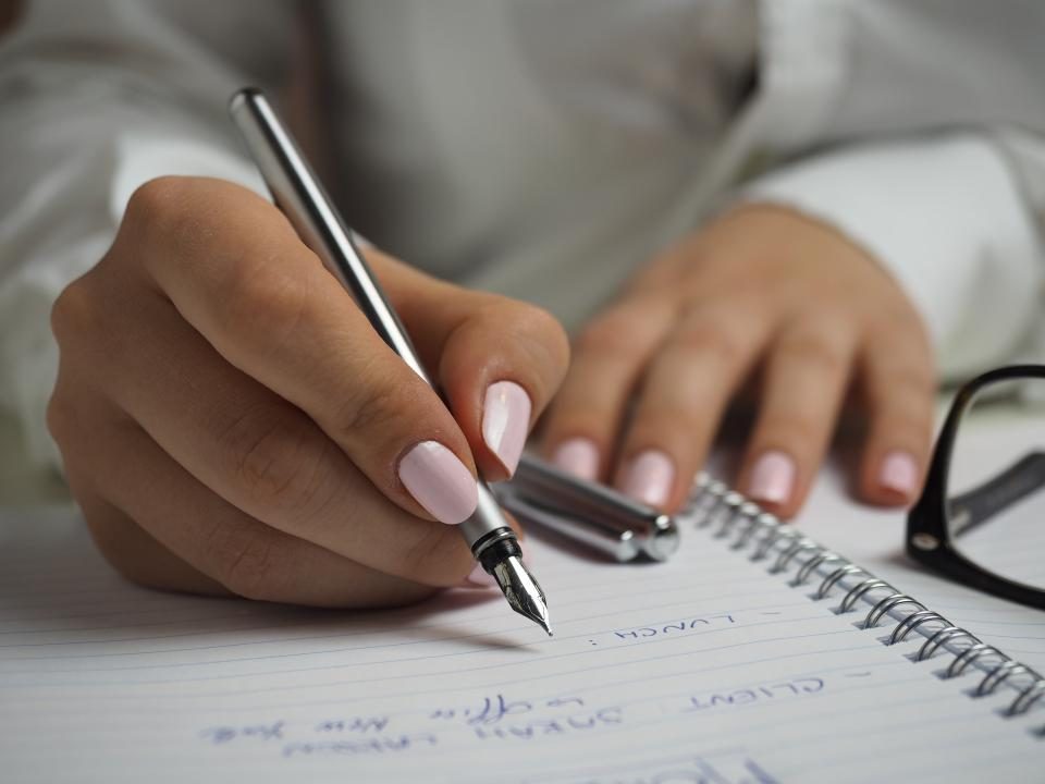 Mão escrevendo num caderno com caneta tinteiro