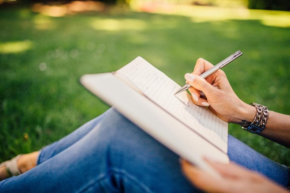 Mão escrevendo num caderno, ao ar livre, sobre a grama