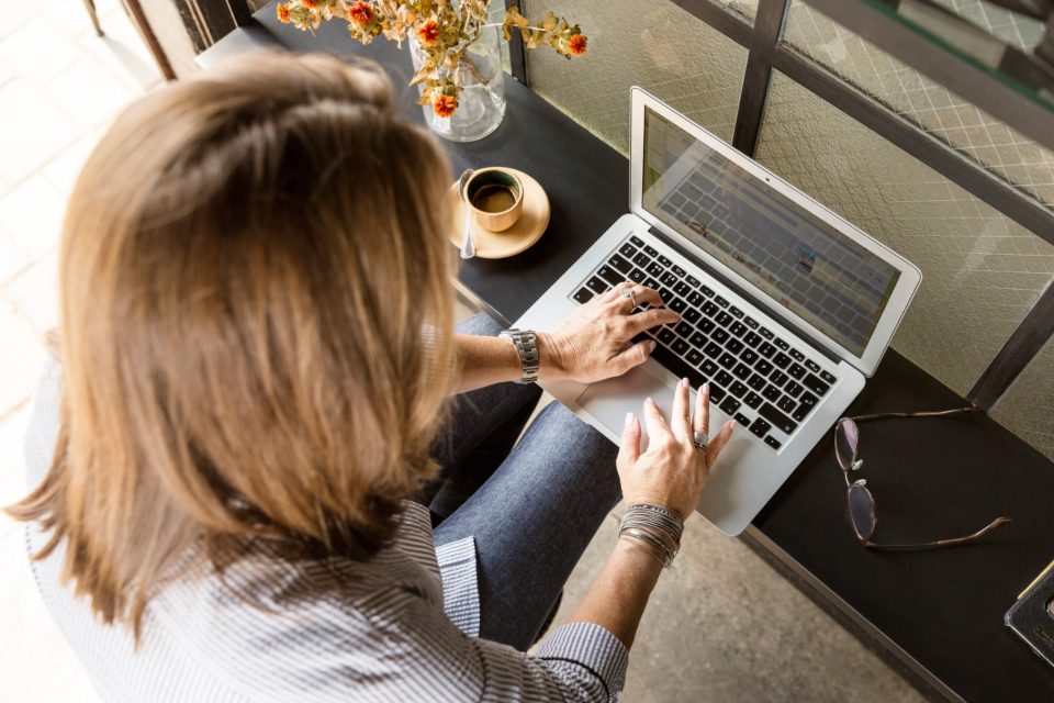 Mulher digitando no notebook sentada em uma poltrona, com o celular na mão
