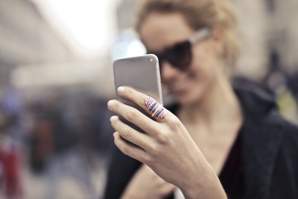 Mulher de óculos escuros segurando o celular para gravar a si mesma