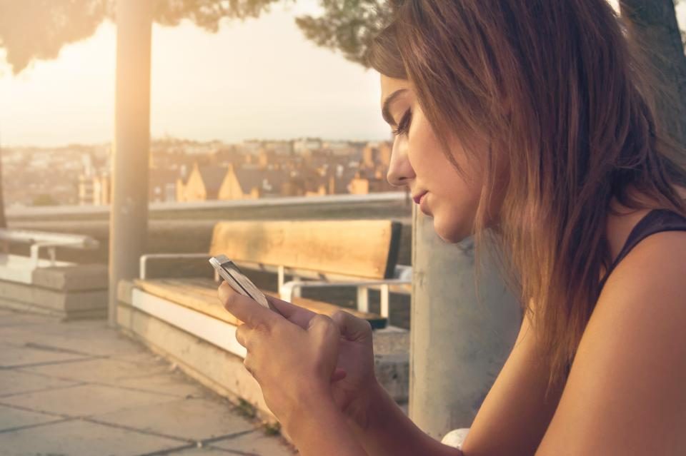 Mulher lendo o celular ao ar livre, no fim da tarde