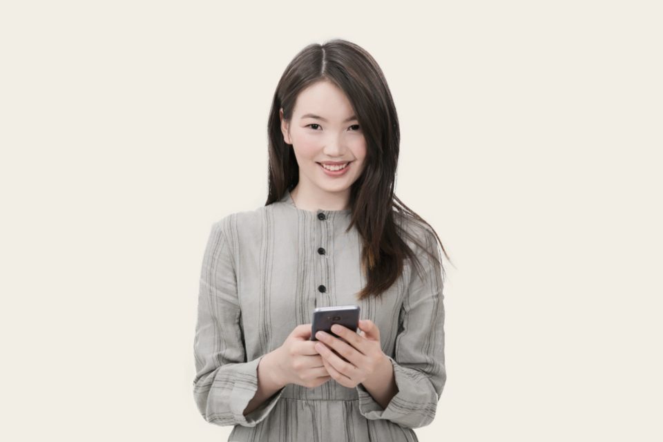 Mulher sorrindo e segurando o celular, diante de um fundo claro