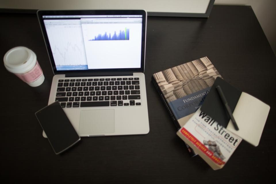 Notebook com gráficos na tela sobre uma mesa escura, com celular e copo de café