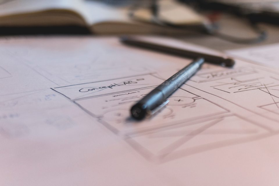 Rascunho de telas de um site desenhado à mão no papel, com uma caneta por cima