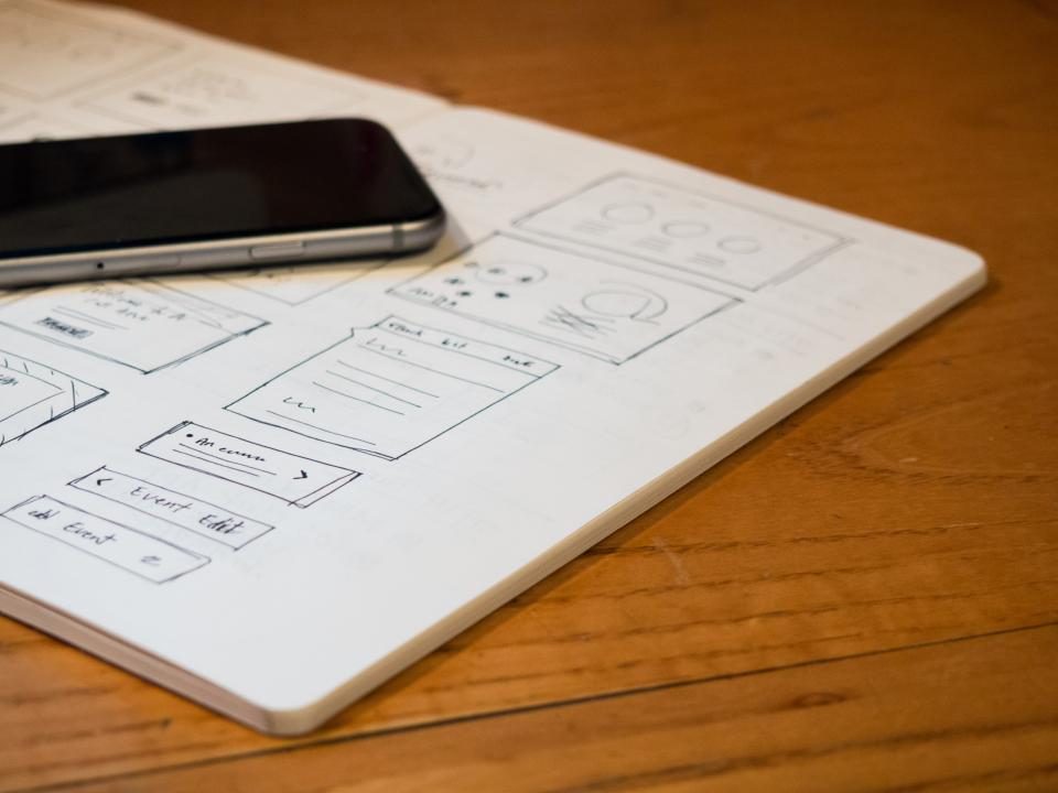 Caderno com rascunhos de telas de site desenhados à mão, ao lado de um celular