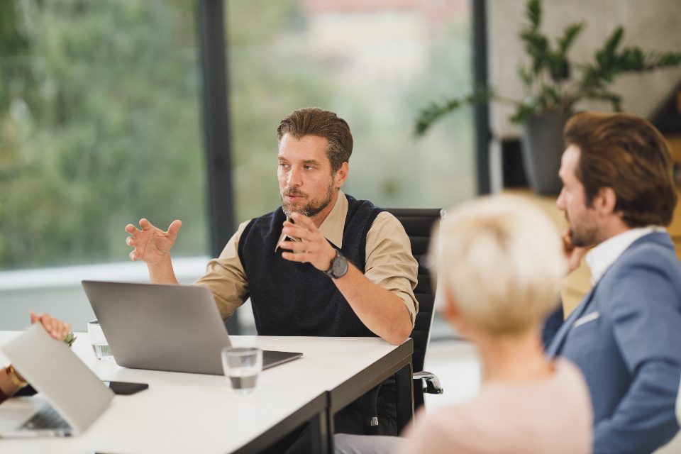 Reunião de trabalho com um homem explicando um projeto para colegas em volta de um notebook