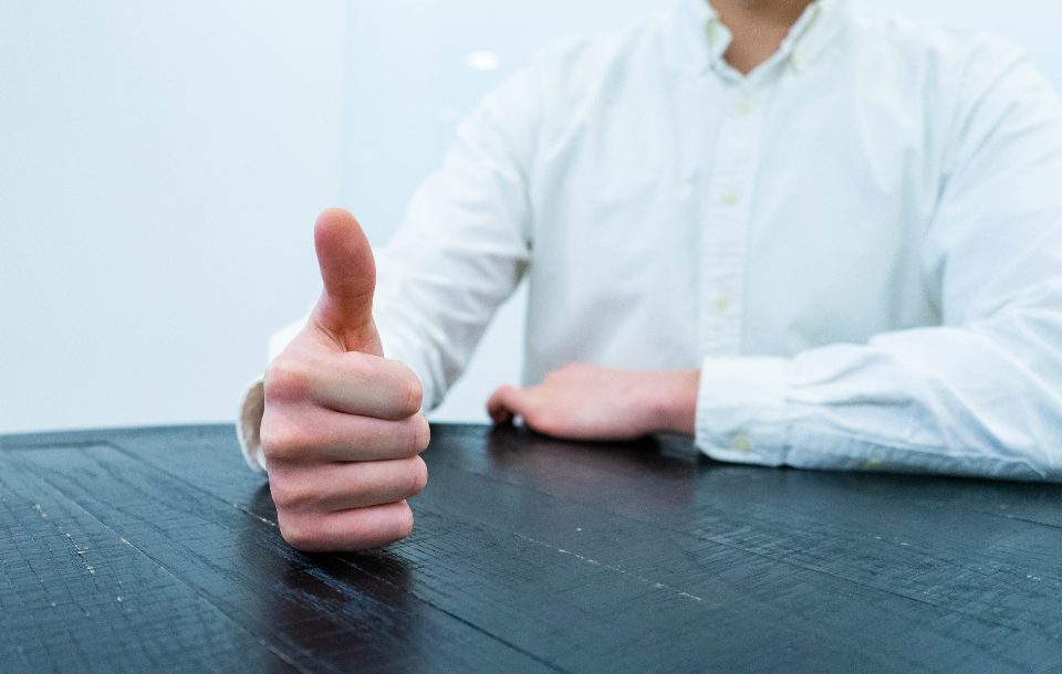 Pessoa fazendo sinal de positivo com o polegar sobre uma mesa
